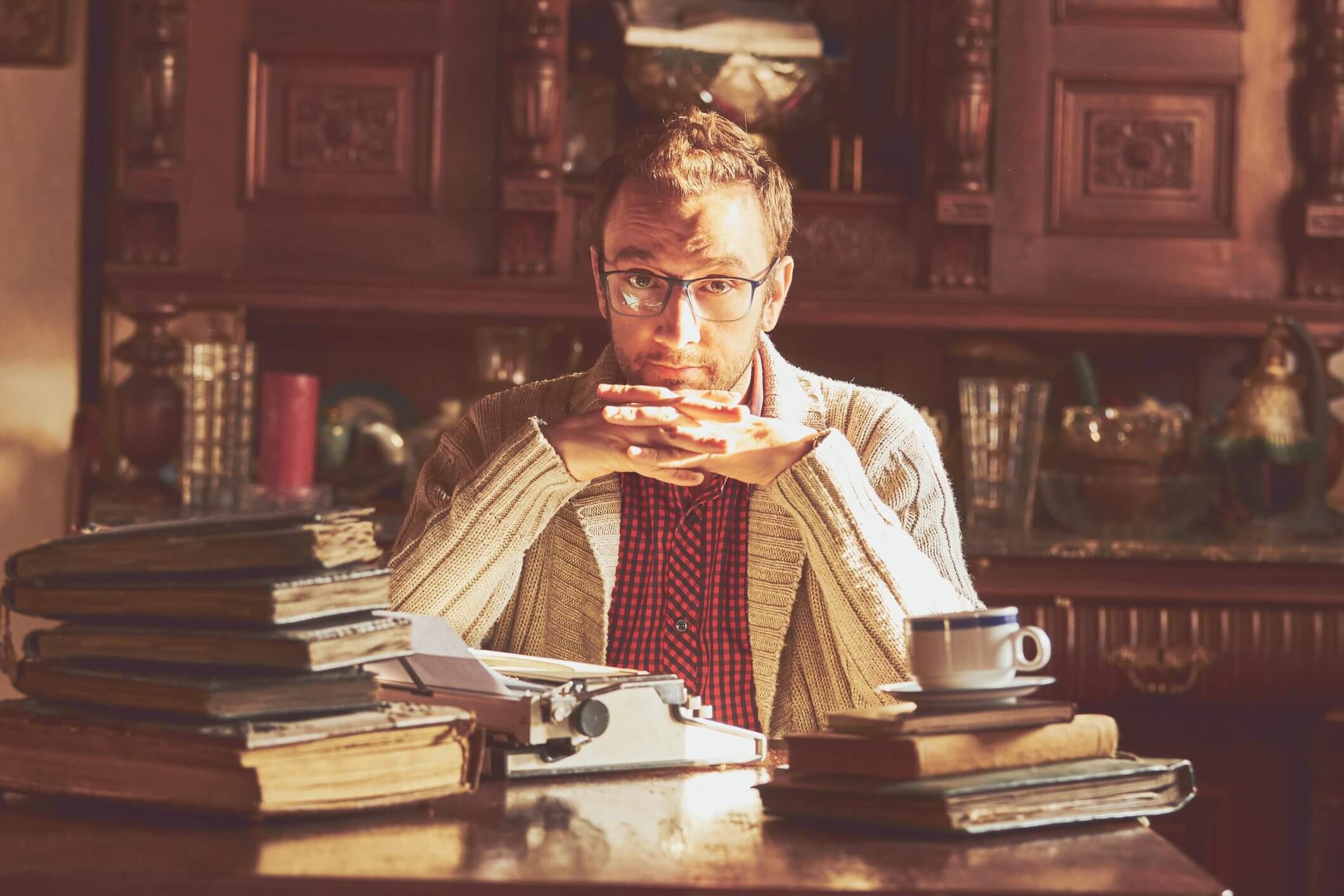 Man pondering at desk with typewriter.